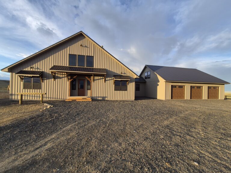 Custom Laramie Wyoming home with textured taupe metal siding, black roof, garage doors, and warm sunset lighting.