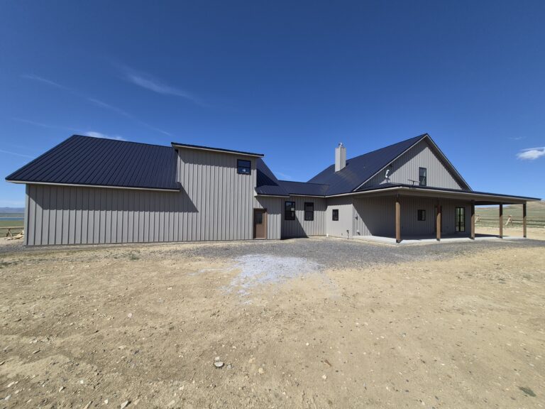 Covered porch with textured taupe metal soffit, wood posts, and open Wyoming hillside view beyond the home.