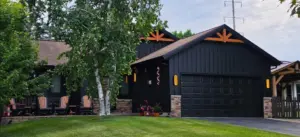 Black metal batten garage exterior with stone accents, warm wood trusses, and a manicured lawn.