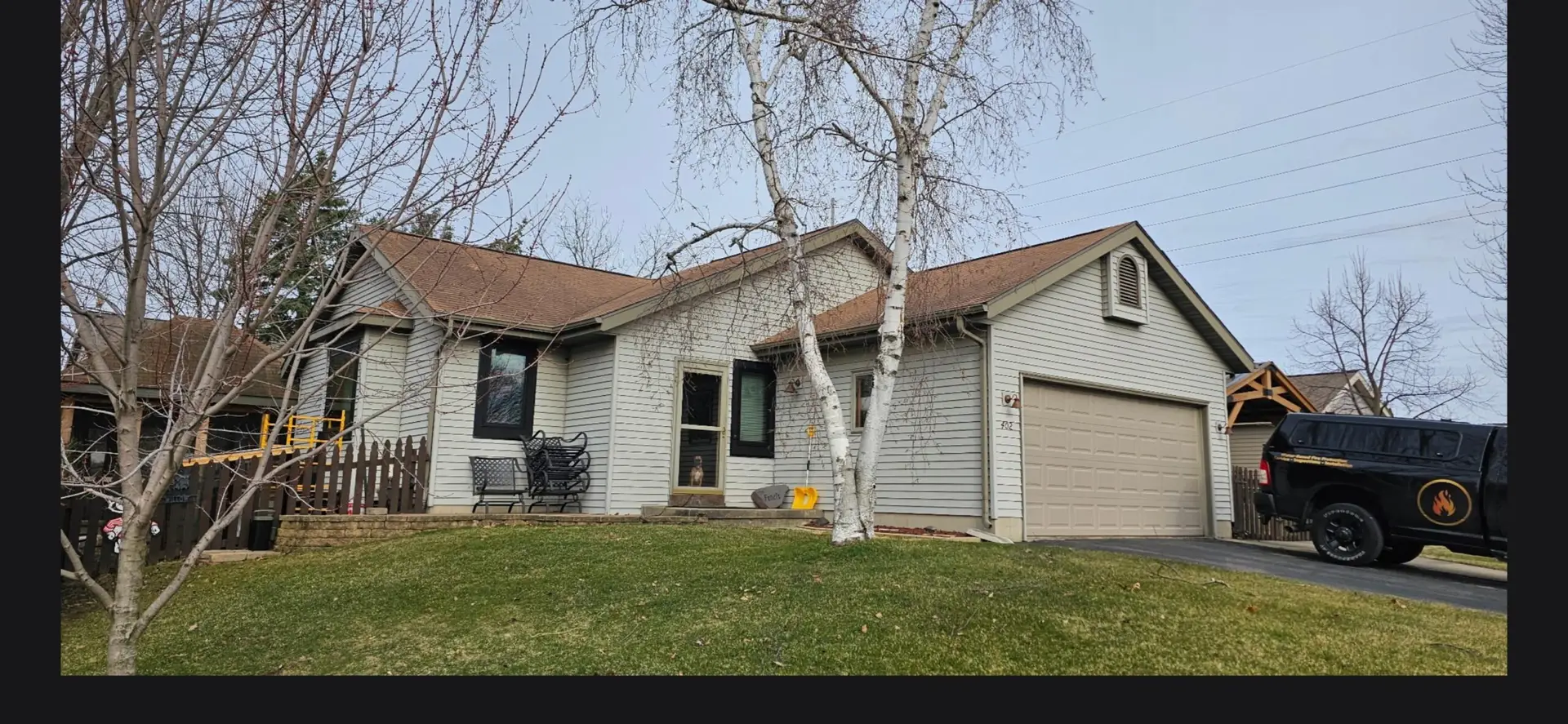 Tan vinyl siding garage before remodel with two white birch trees and tan garage door.